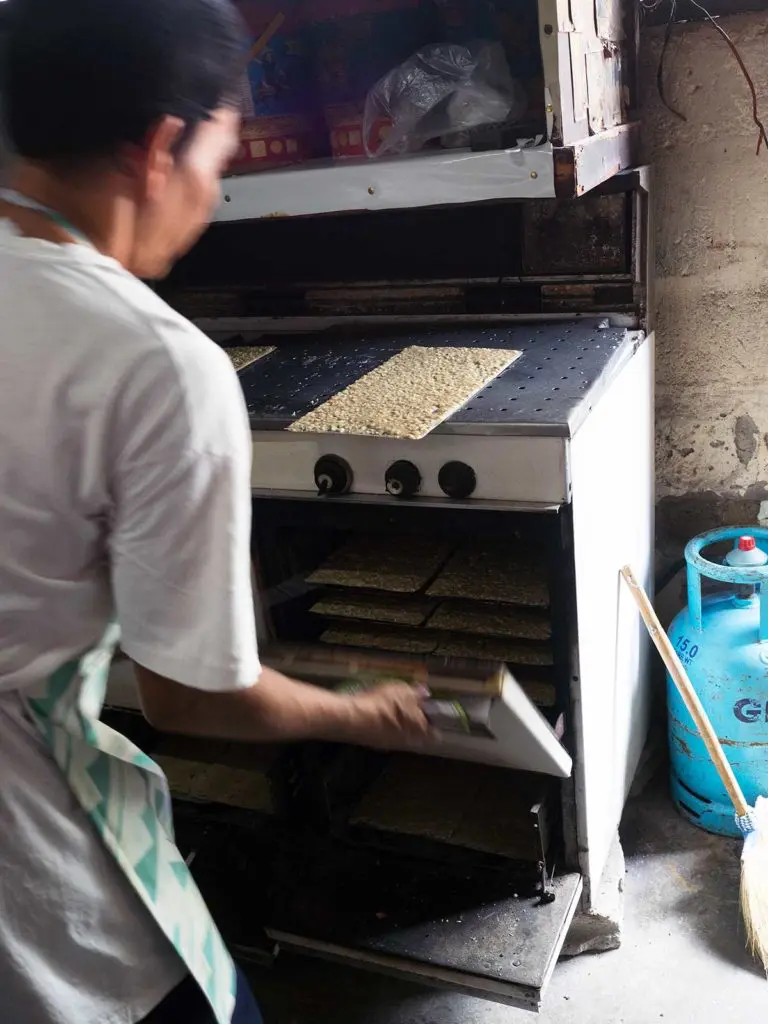 man placing sheets of cashew meringue in the oven to bake