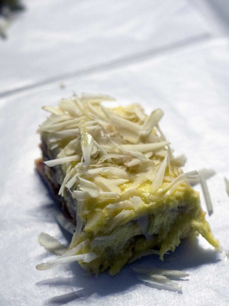 a rectangular piece of sans rival cake topped with shaved cashew