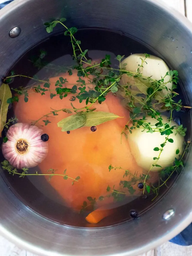 corned beef in a large pot with anion, garlic and herbs, covered with water ready to cook