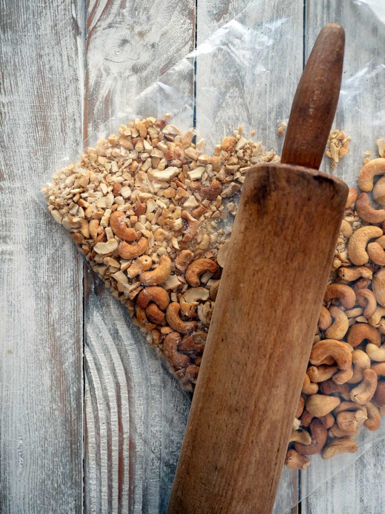 roasted cashews in a zip lock back being crushed with a wooden rolling pin