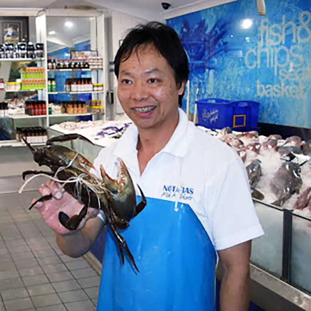 fishmonger in a fish shop holding a live large mud crab