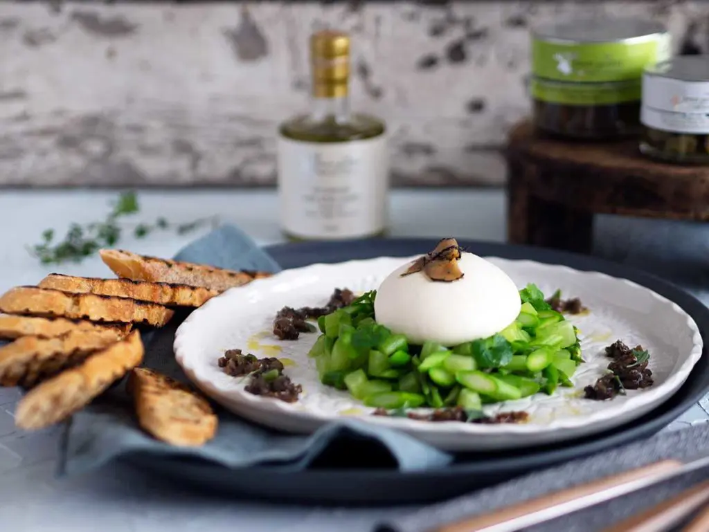 burrata on a bed of asparagus and celery, topped with truffle carpaccio, salsa tartufata dolloped around the outside on a white plate