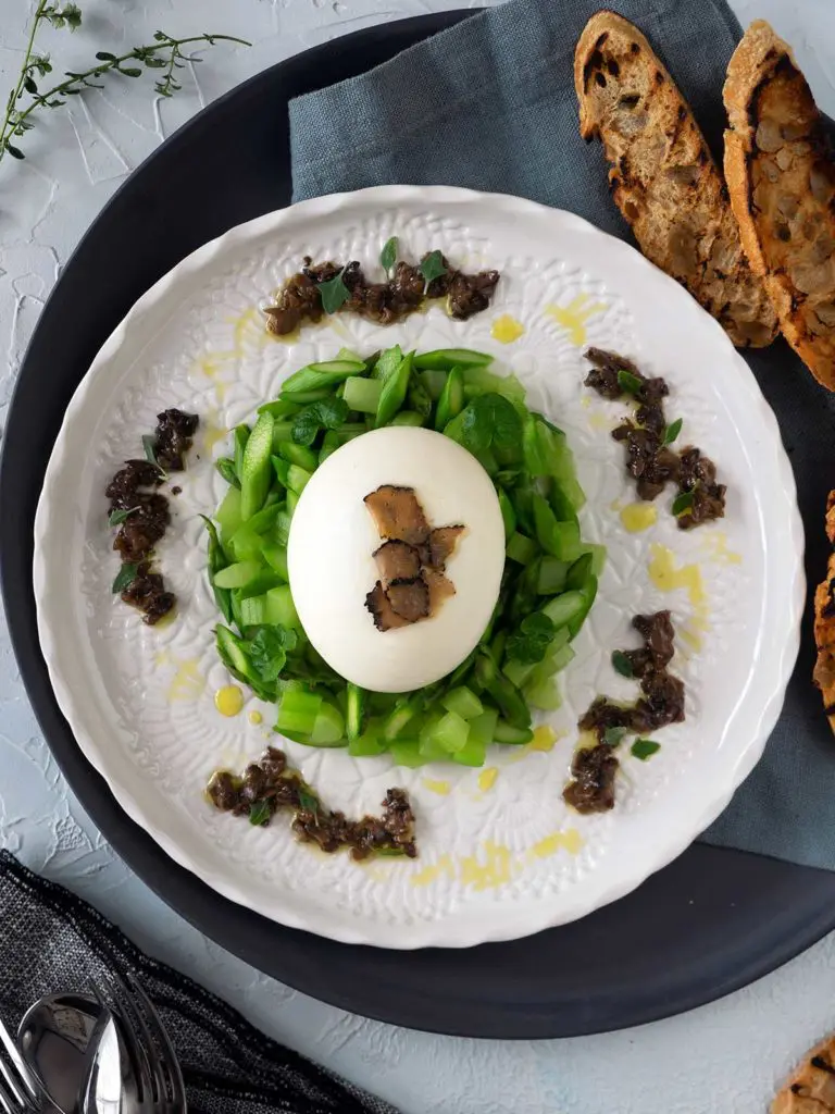 burrata on a bed of asparagus and celery, topped with truffle carpaccio, salsa tartufata dolloped around the outside on a white plate