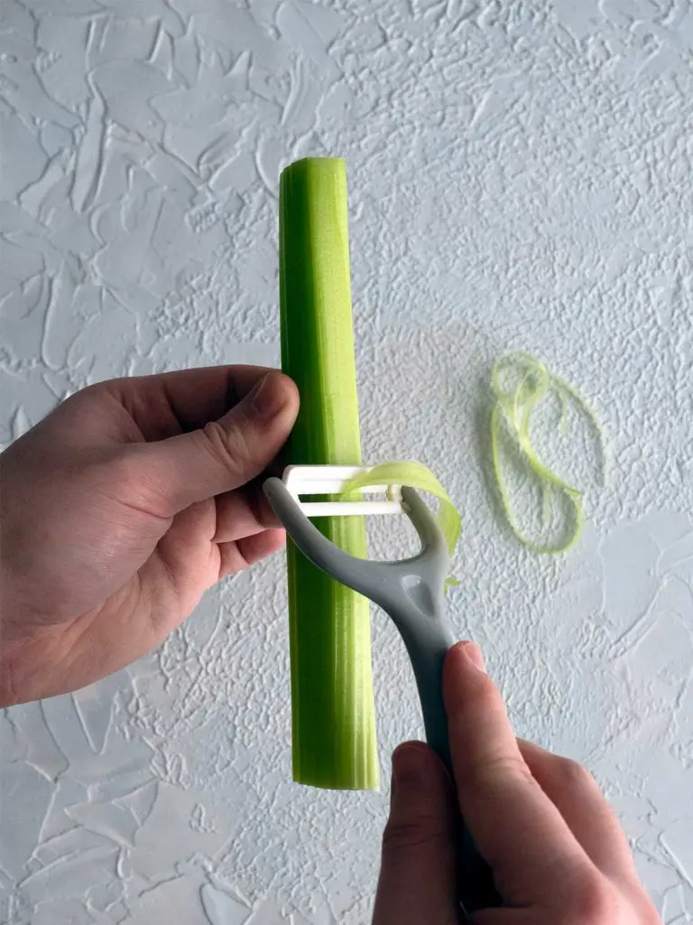 string being removed from a stick of celery by a vegetable peeler