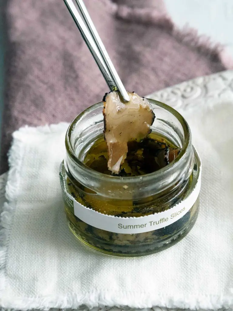 a slice of truffle carpaccio being removed from a jar by styling tweezers