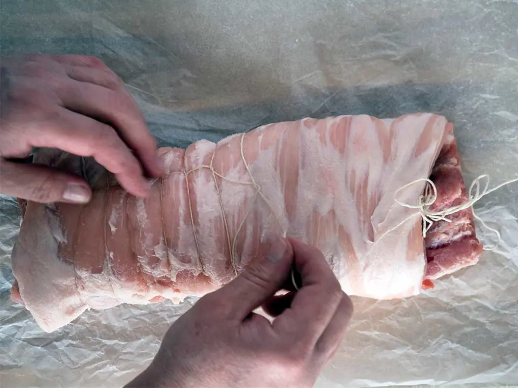 tying a rolled piece of pork belly with string
