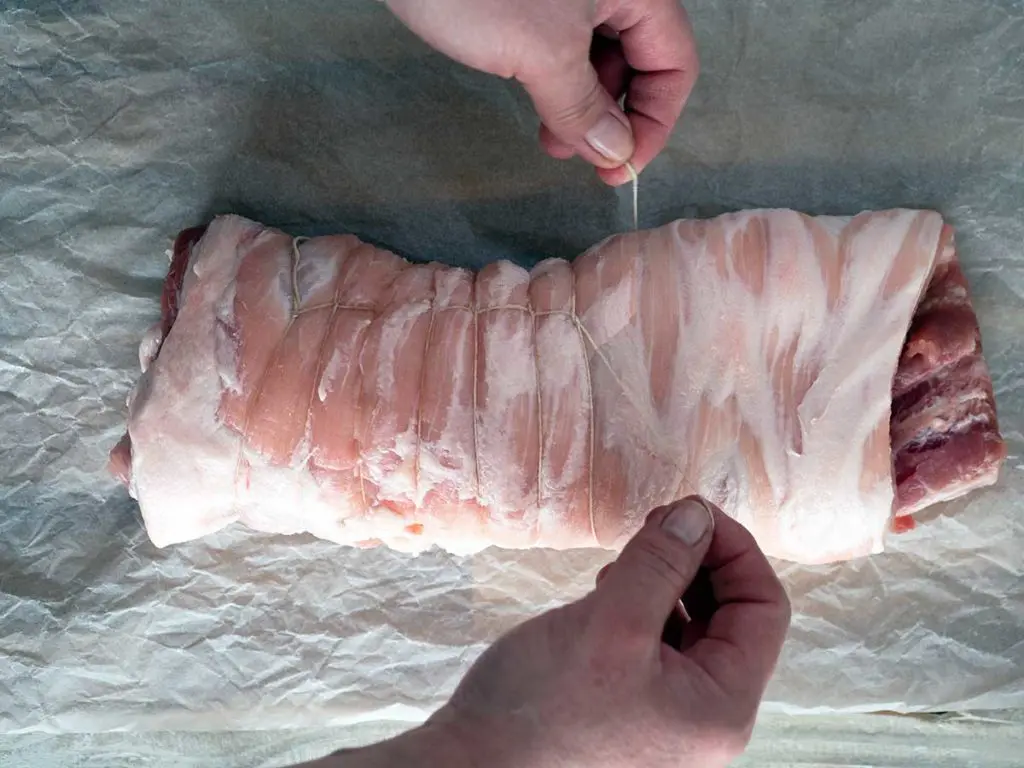 tying a rolled piece of pork belly with string