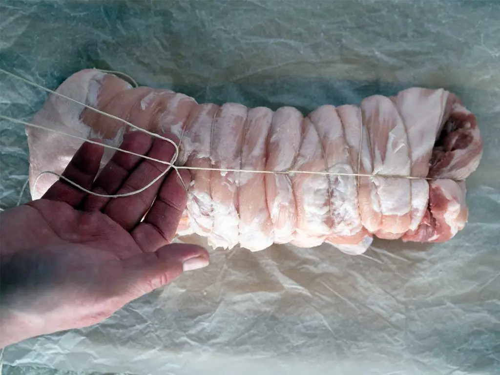 tying a rolled piece of pork belly with string