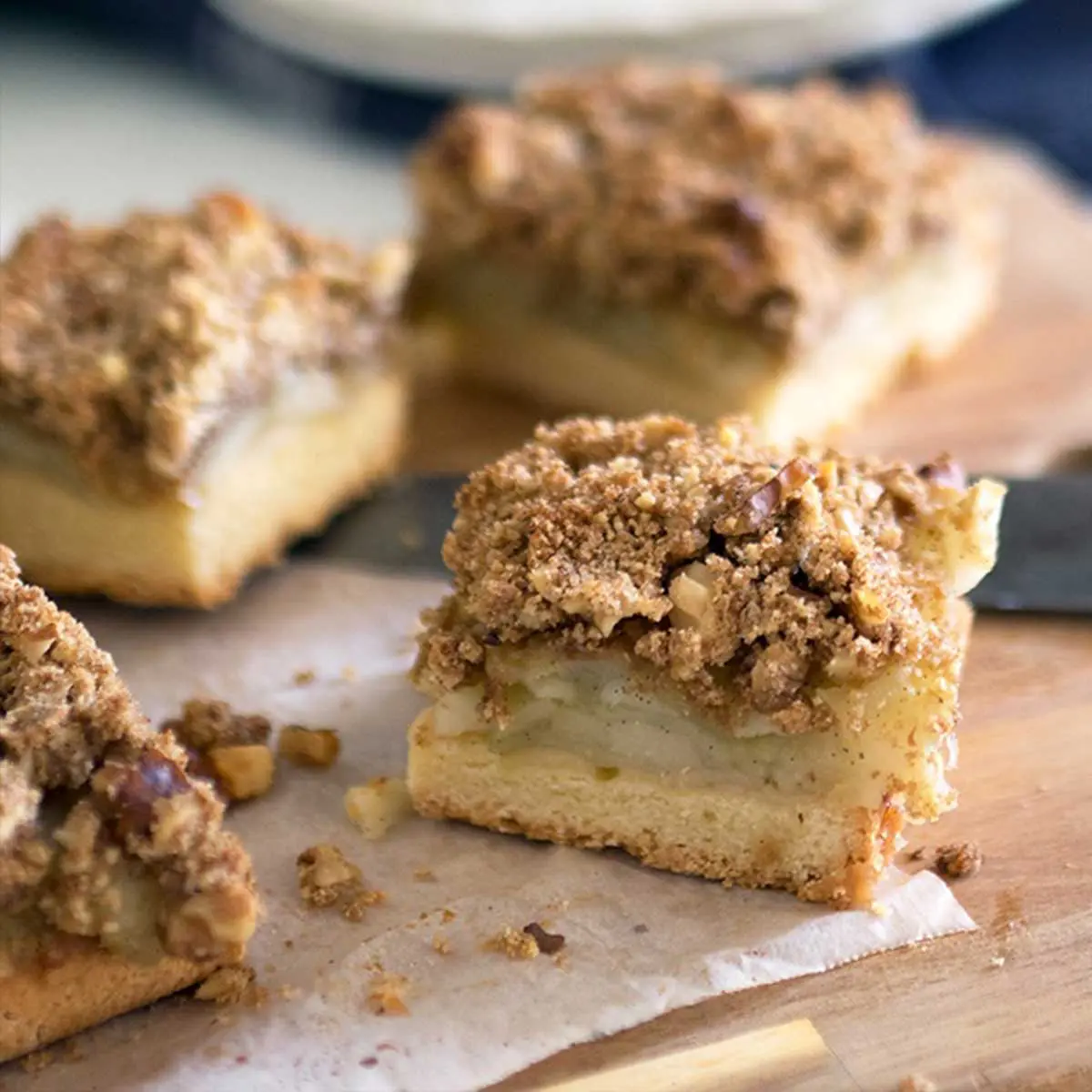 four slices of apple crumble slice on parchment paper with a wood background
