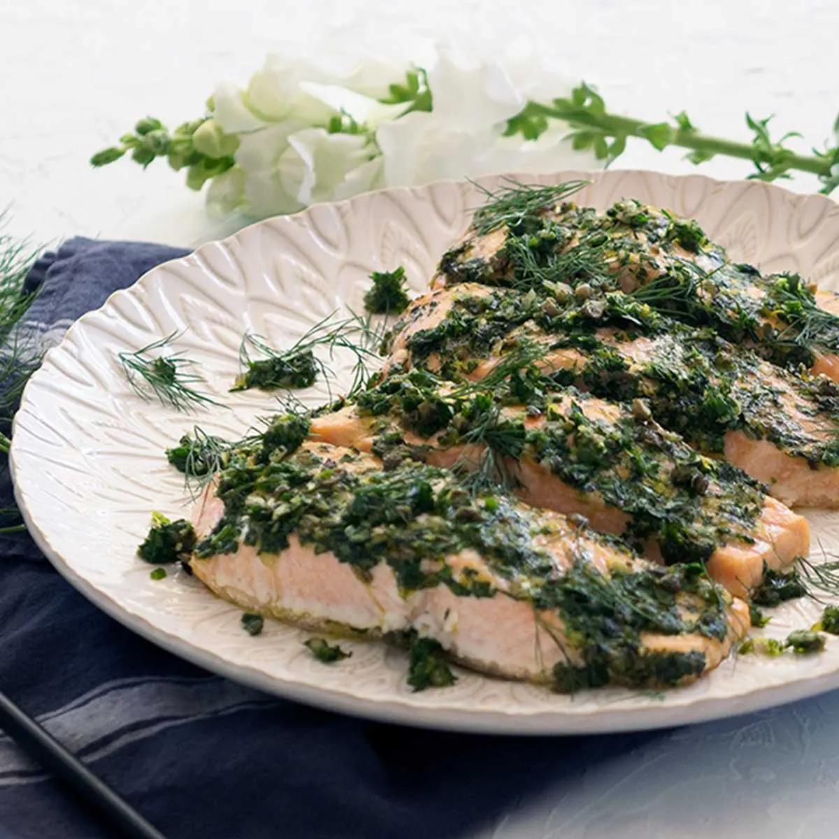 Herb encrusted salmon fillets on a white plate, white flower in the background.