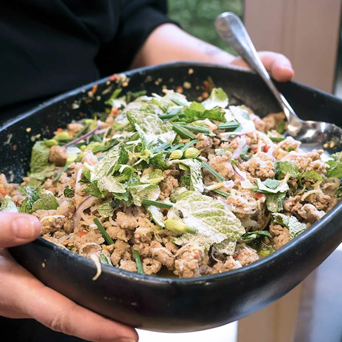 Minced duck with herbs and chilli in a black bowl held by hands.