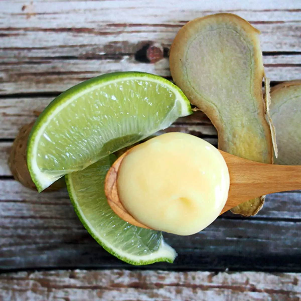 A spoon with Curd resting on some lime and slices of ginger against a wooden background.
