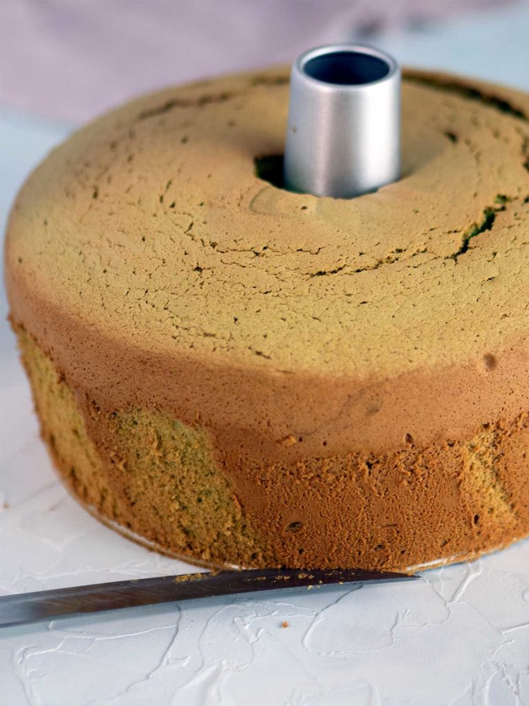 knife being inserted between bottom of cake and base of tin to remove cake from tin