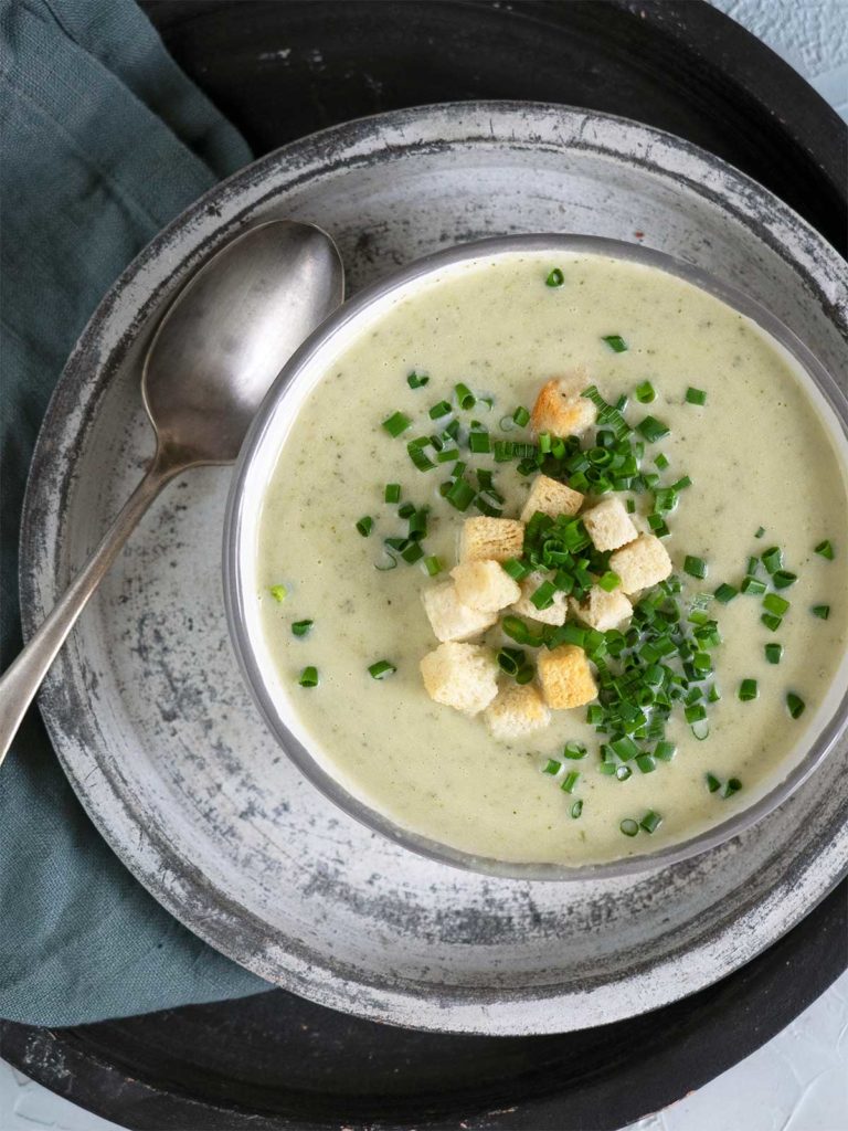 Broccoli and cauliflower soup topped with croutons and chives in a bowl with a spoon on the side.