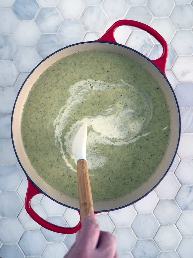 Cream being stirred into the soup in a pot.