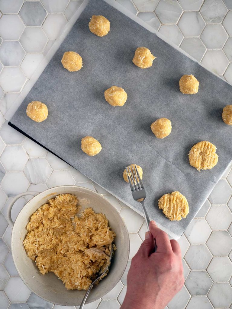 cookie dough balls on a baking sheet being flattened by a fork