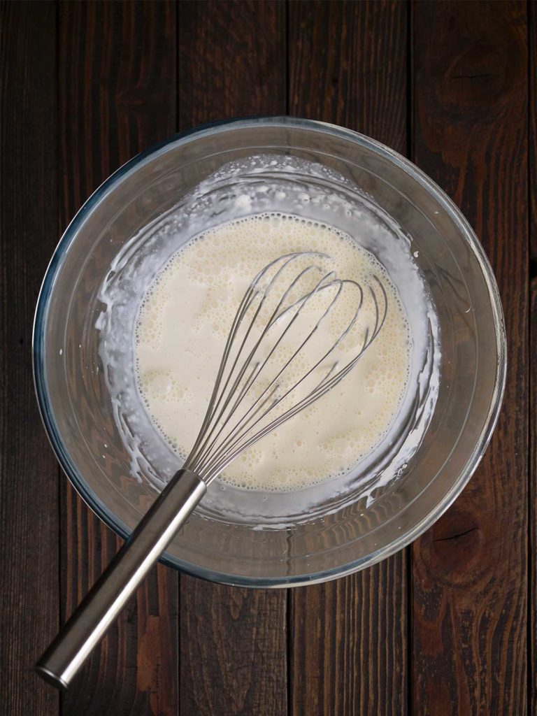 cream mixture being whisked together in a glass bowl