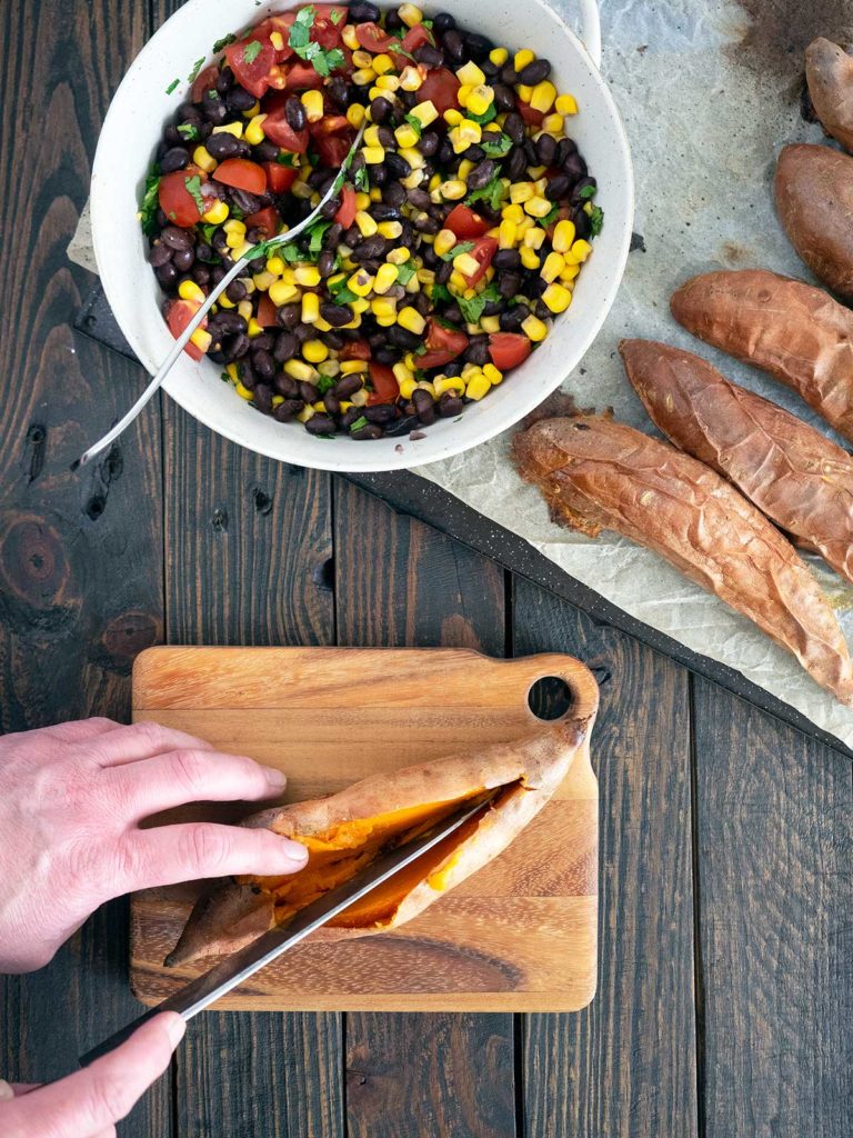 cutting open baked sweet potatoes on a wooden board
