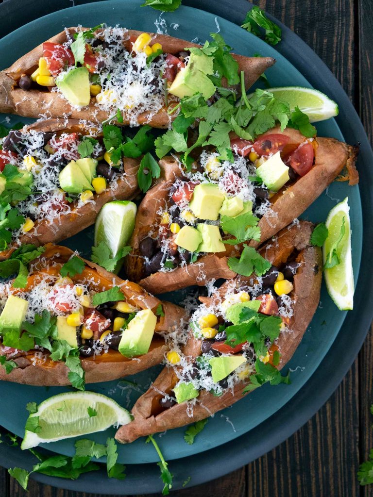 baked sweet potatoes cut open and stuffed with various fresh ingredients on a plate