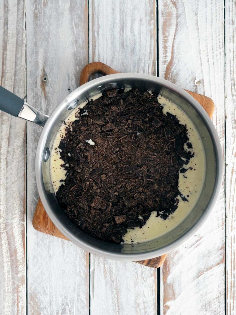 grated chocolate added to warm cream in pot on a wooden board