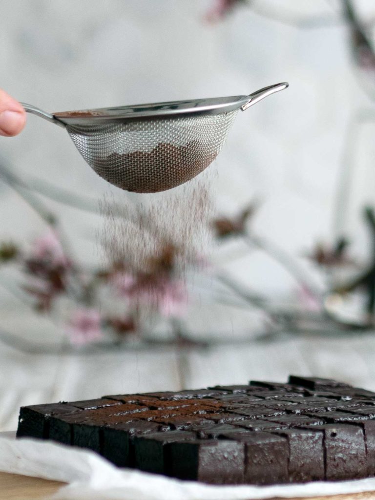 cocoa powder in a sieve being dusted over cut nama chocolate