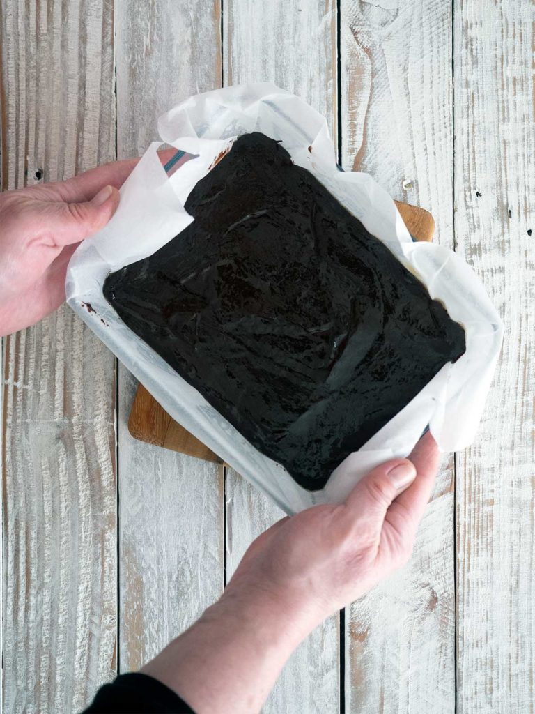 tapping the lined tray filled with melted chocolate mixture on the wooden board