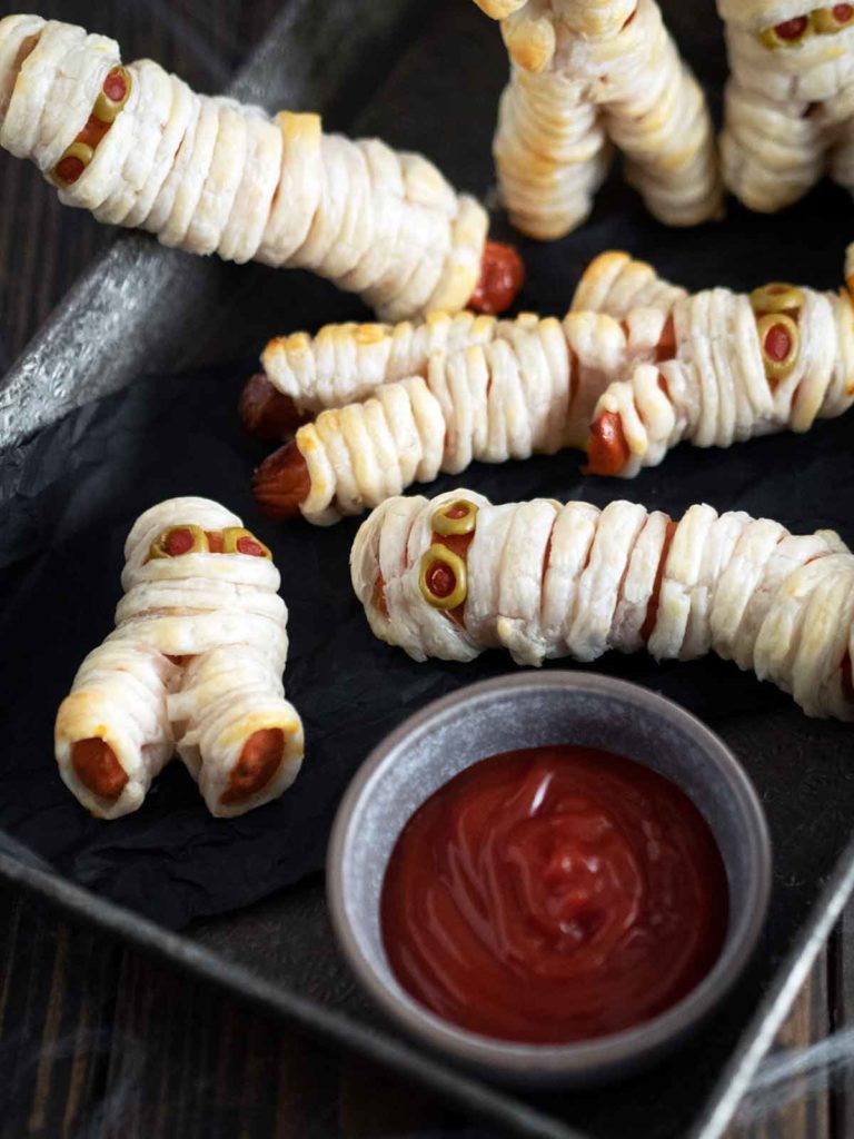 mummy hot dogs in a tray with a bowl of tomato ketchup