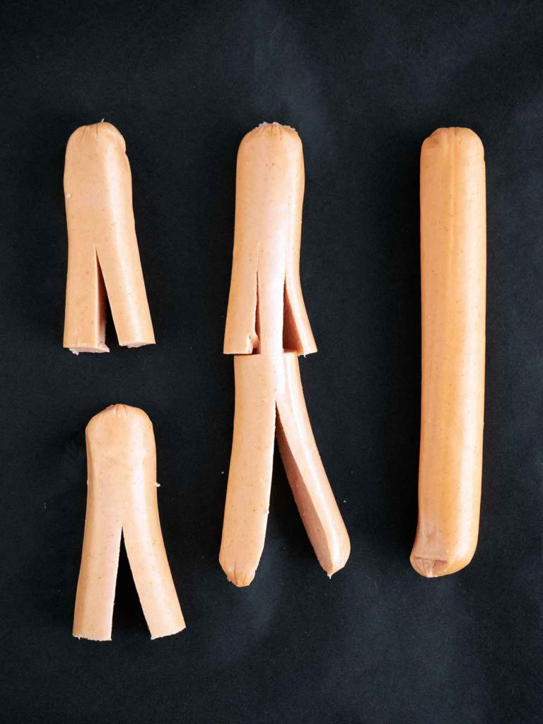 hot dogs cut into mummy shapes on black paper