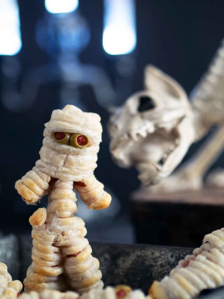 hot dog mummy with arms and legs and cat skeleton in the background