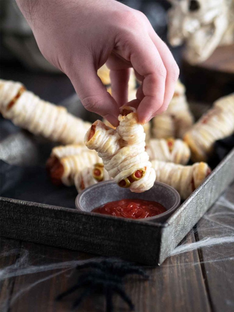 hand dunking mini mummy in sauce