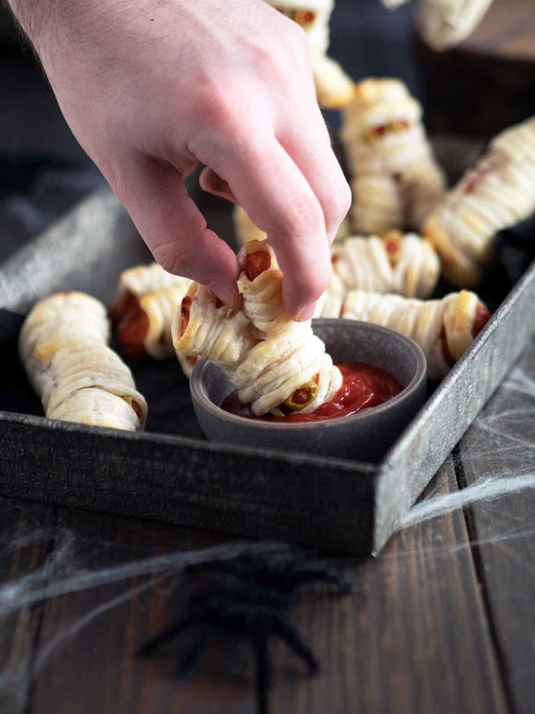 hand dunking mini mummy in sauce