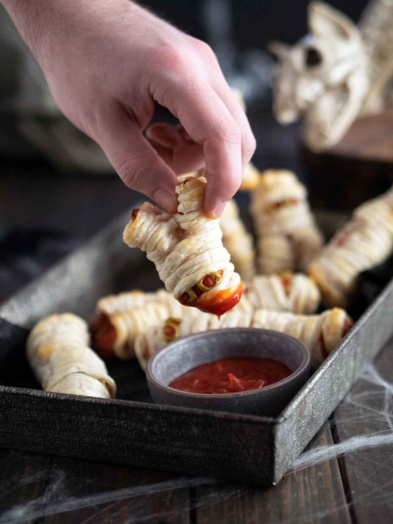hand dunking mini mummy in sauce