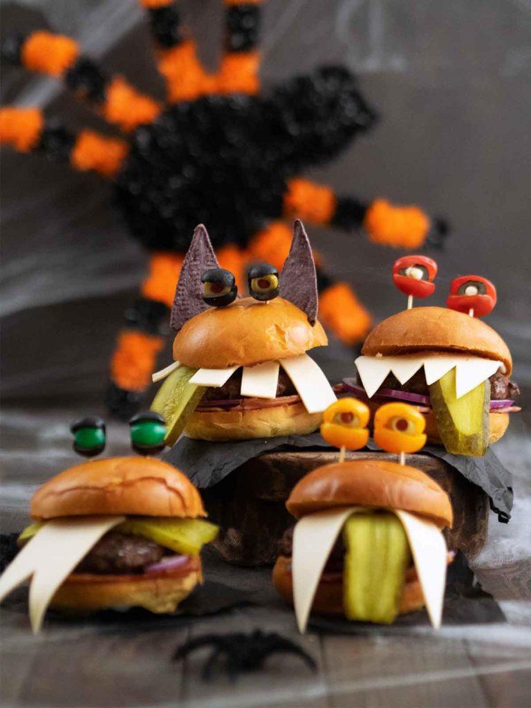 four monster burgers grouped together with a big black and orange spider in the background