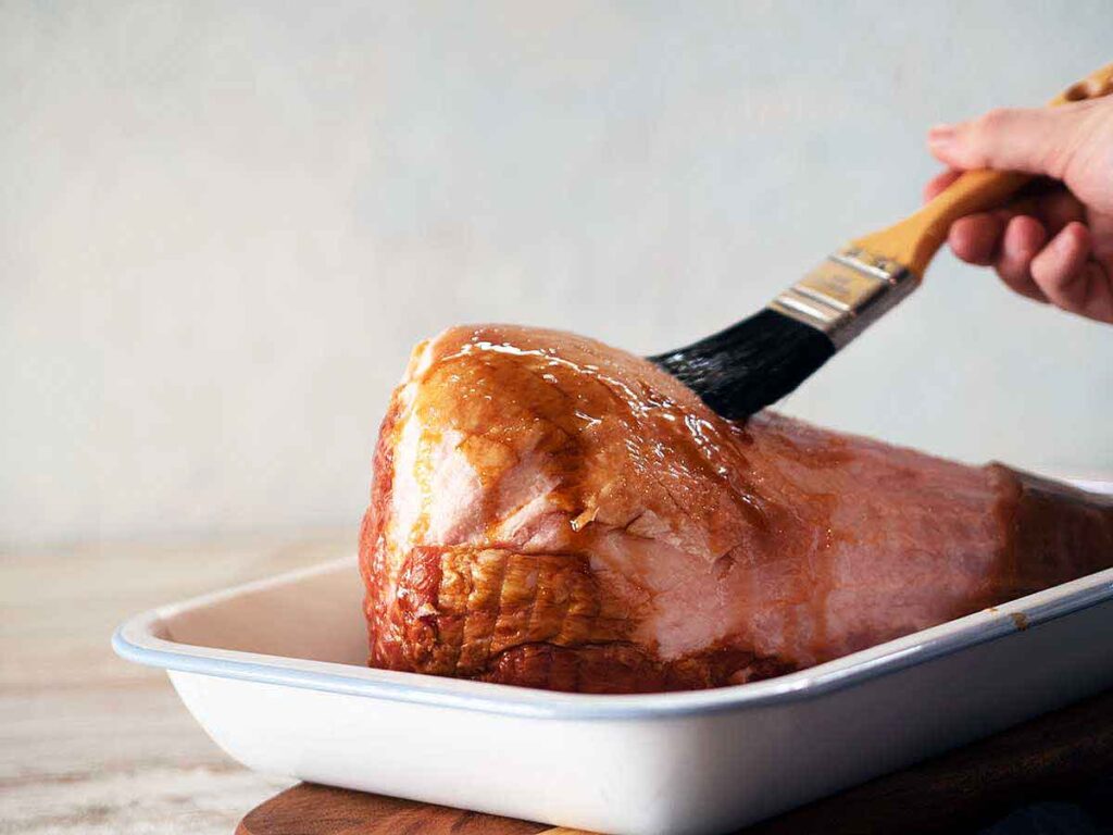 ham in a baking tray being brushed with glaze
