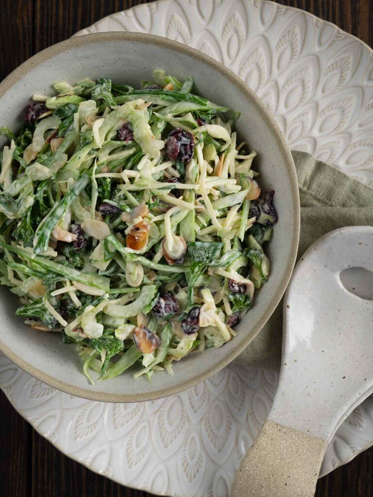 finished recipe in a ceramic serving dish on top of a large plate with salad servers next to the bowl