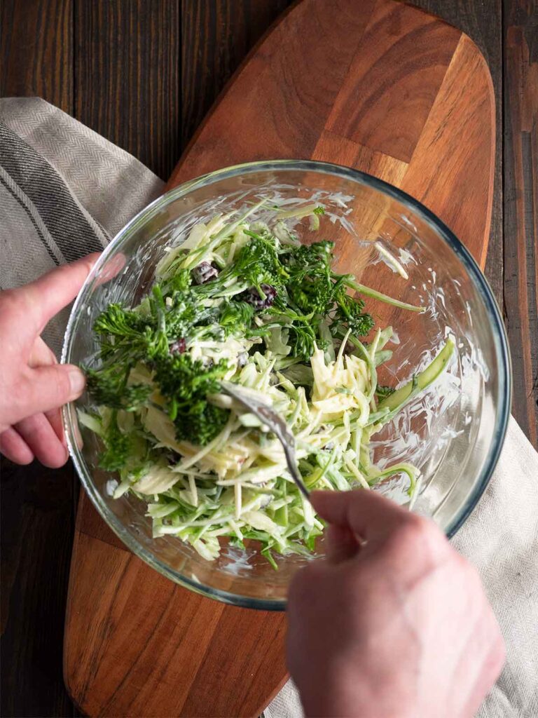 mixing dressing into the salad ingredients in a glass bowl