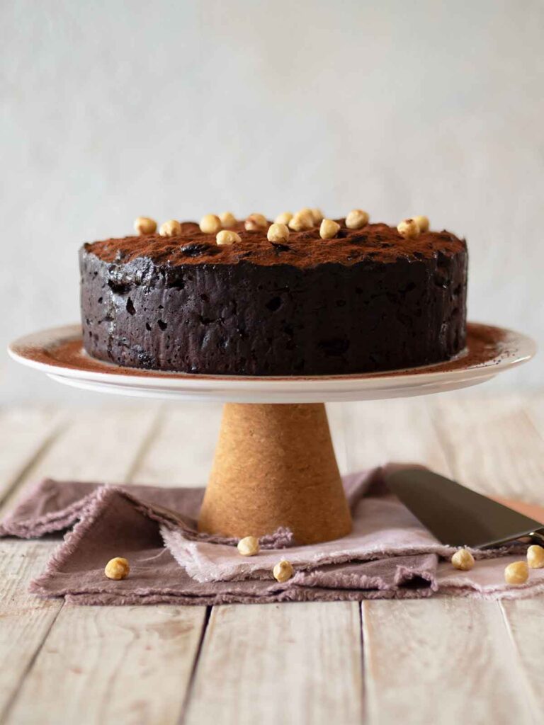 cake on a cake stand decorated with cocoa powder and roasted hazelnuts