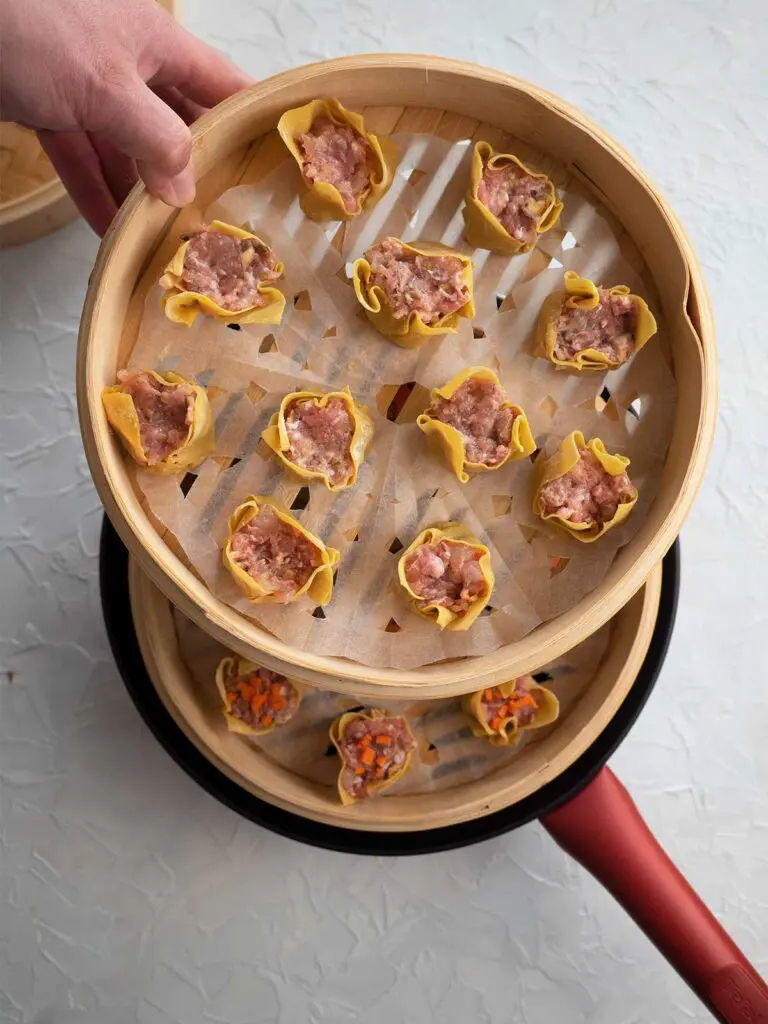 a person stacking another basket with dumplings on top of basket already sitting in wok