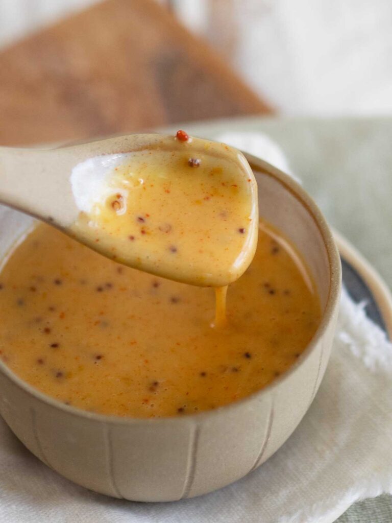 honey mustard dressing dripping off a spoon into a small serving bowl