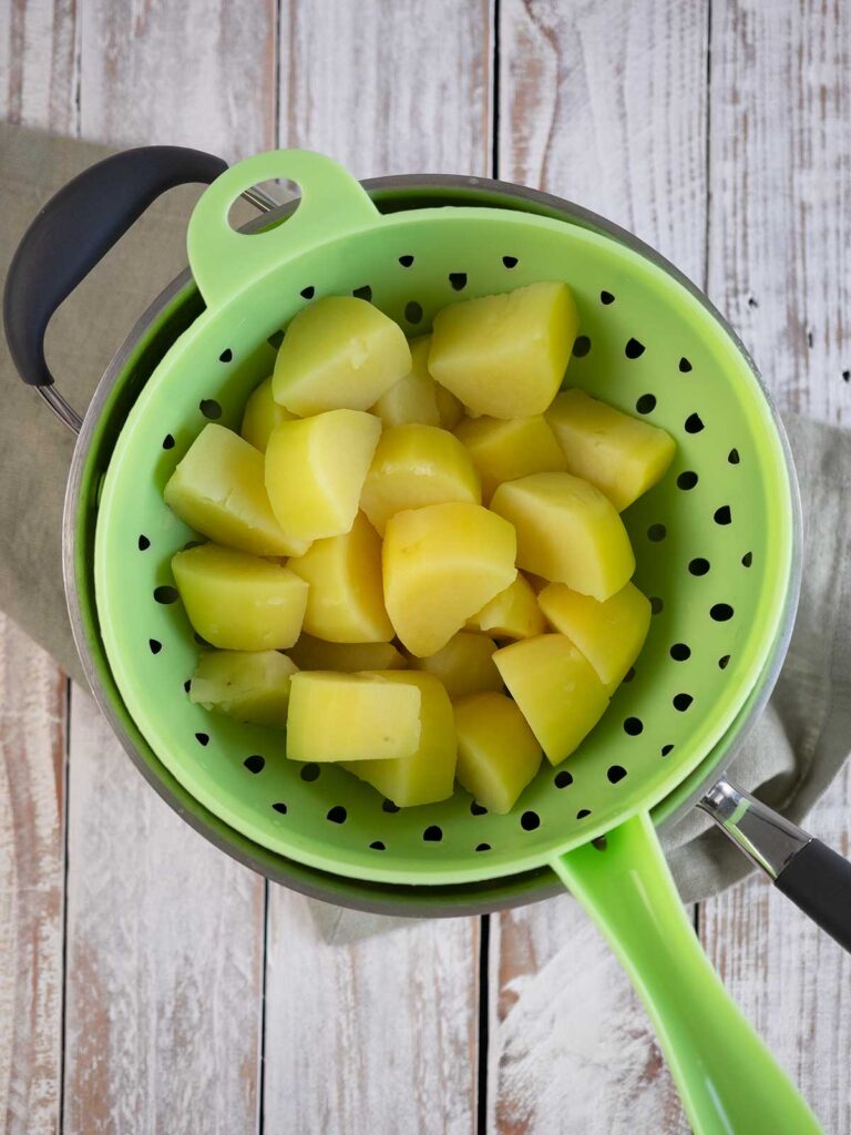 boiled potatoes in a green drainer sittintg on the po
