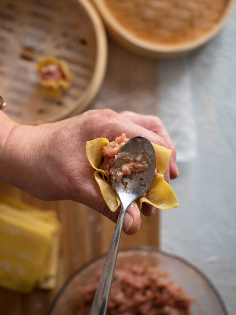 wonton wrapper being wrapped around dumpling stuffing and being smoothed down by a teaspoon