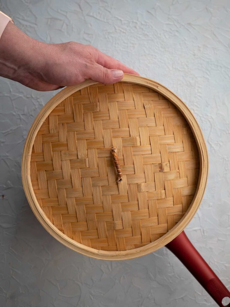 bamboo steamer basket lid being placed on top of the steamer baskets