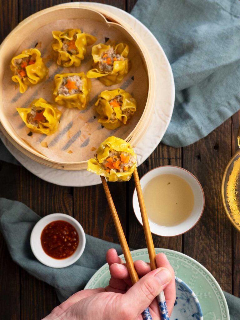 a person removing shumai from steamer basket with chopsticks