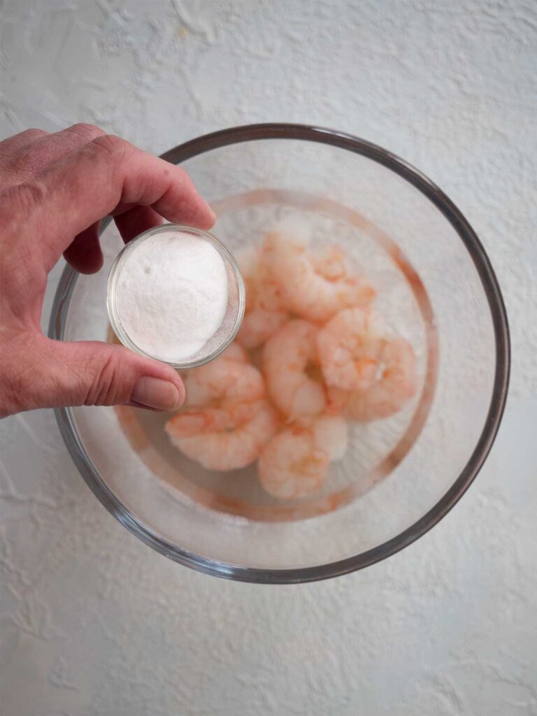 adding baking soda to a bowl with water and prawns