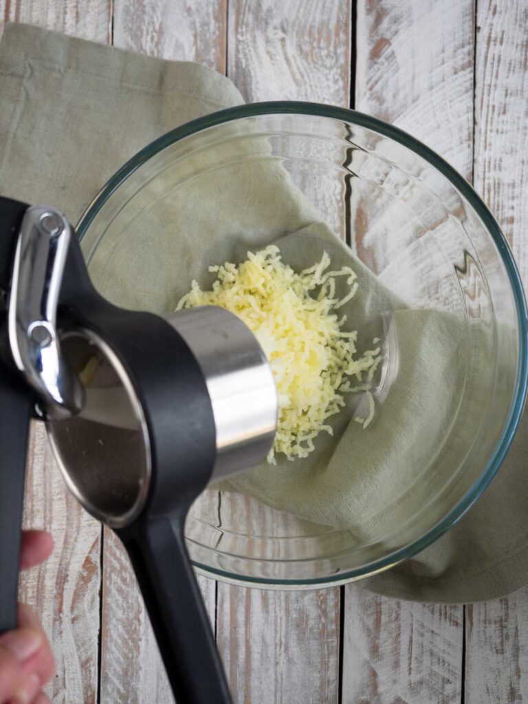 ricer ricing potatoes into a glass bowl