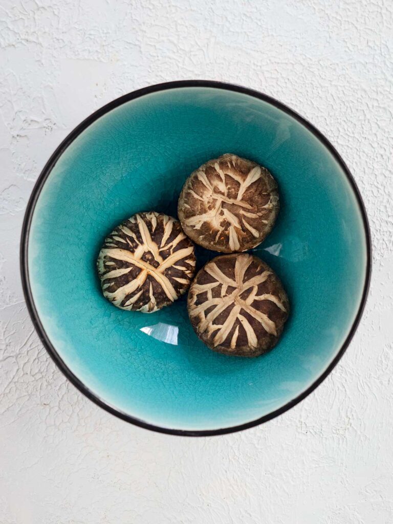 three dried shitake mushrooms in a blue bowl