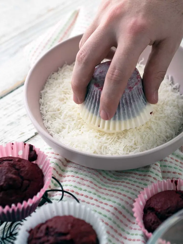 dipping a frosted cupcake in shredded coconut