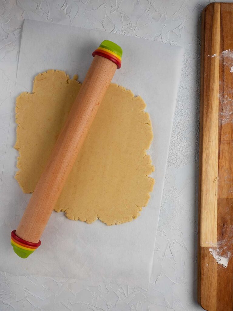 dough being rolled out by a wooden rolling pin