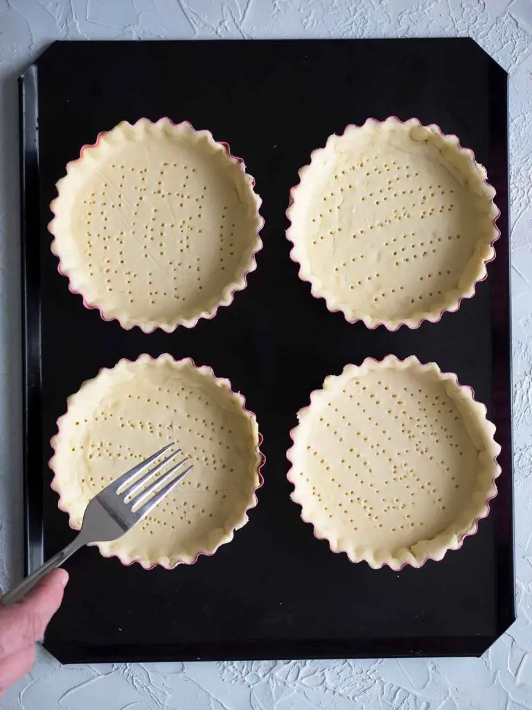 tart shells being pricked by a fork