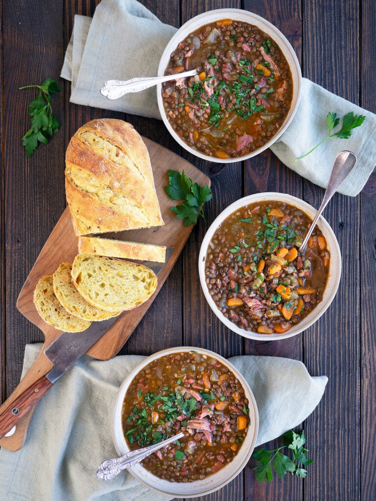 three bowls of soup with a loaf of bread on a cutting board